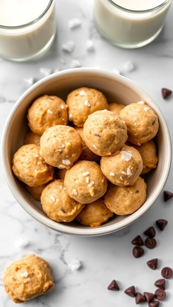 A bowl of no-bake peanut butter cookie dough bites with chocolate chips and sea salt, surrounded by glasses of milk.