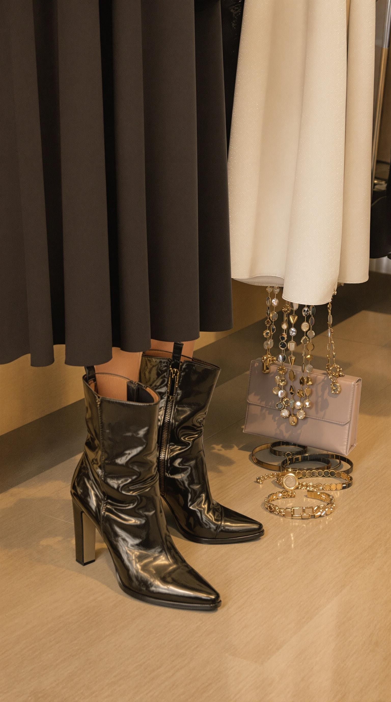 A pair of elegant burgundy dress boots next to a sparkling bracelet and a perfume bottle, set against a soft fabric backdrop.