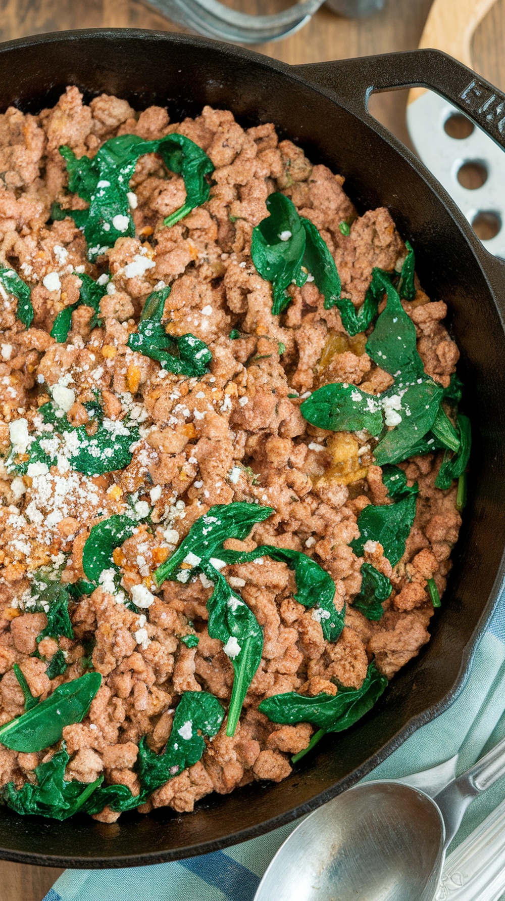 A skillet filled with cooked ground turkey and fresh spinach, garnished with feta cheese.