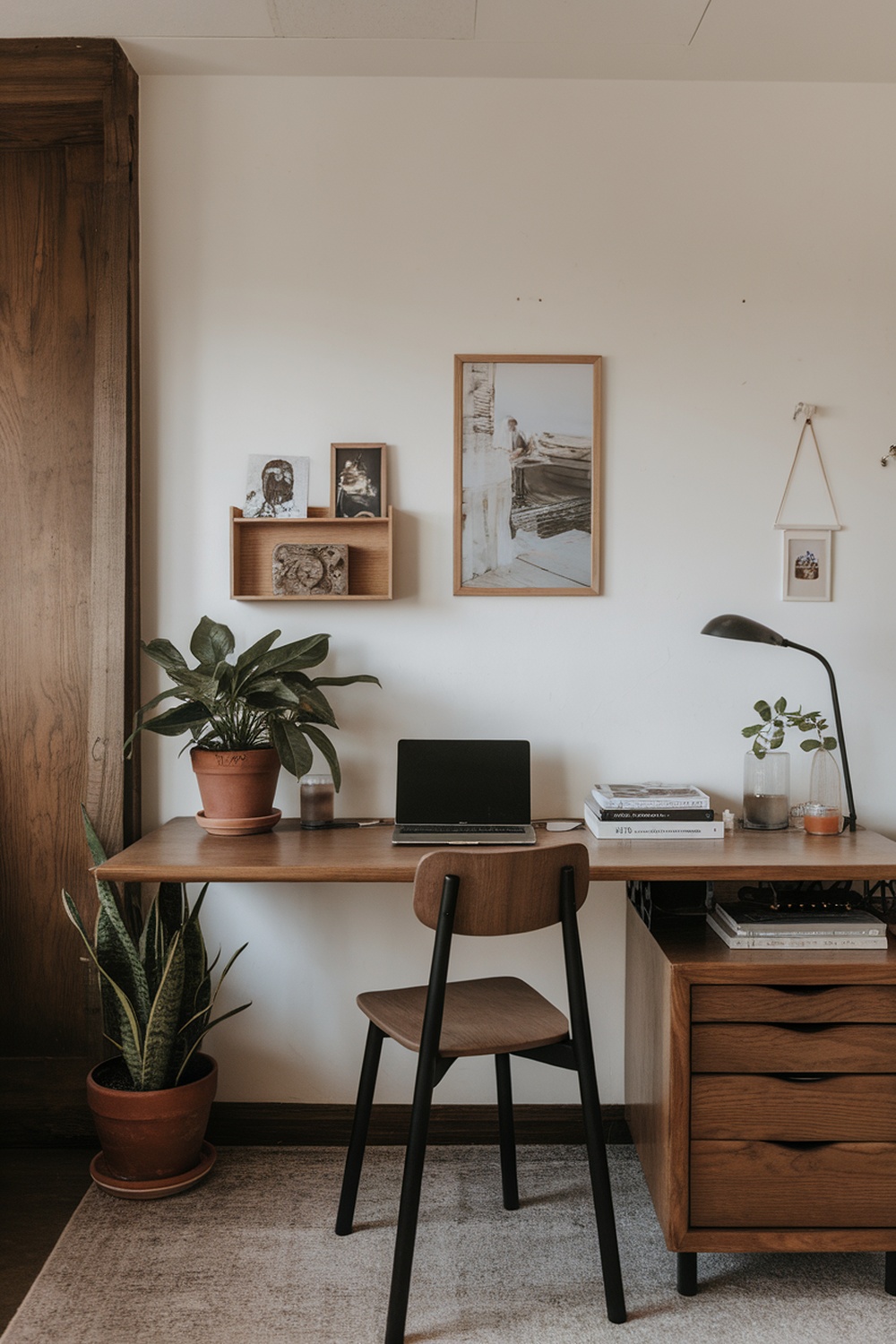 A minimalist home office featuring a wooden desk with a laptop, plants, and personal decorations.