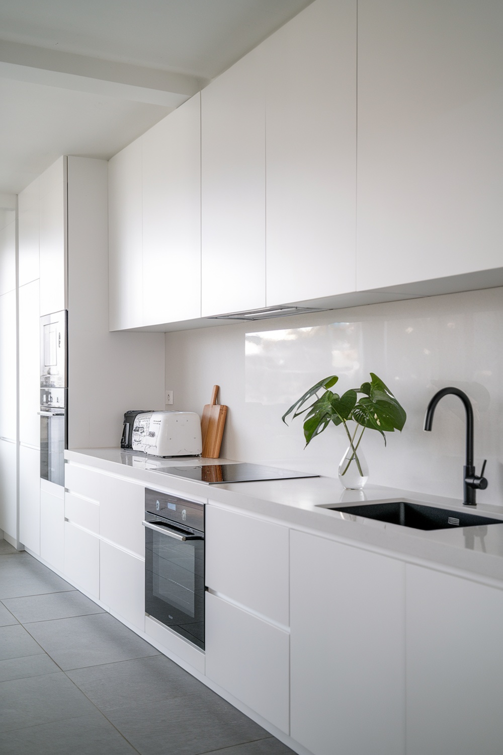 A sleek minimalist white kitchen with modern appliances and a small plant.