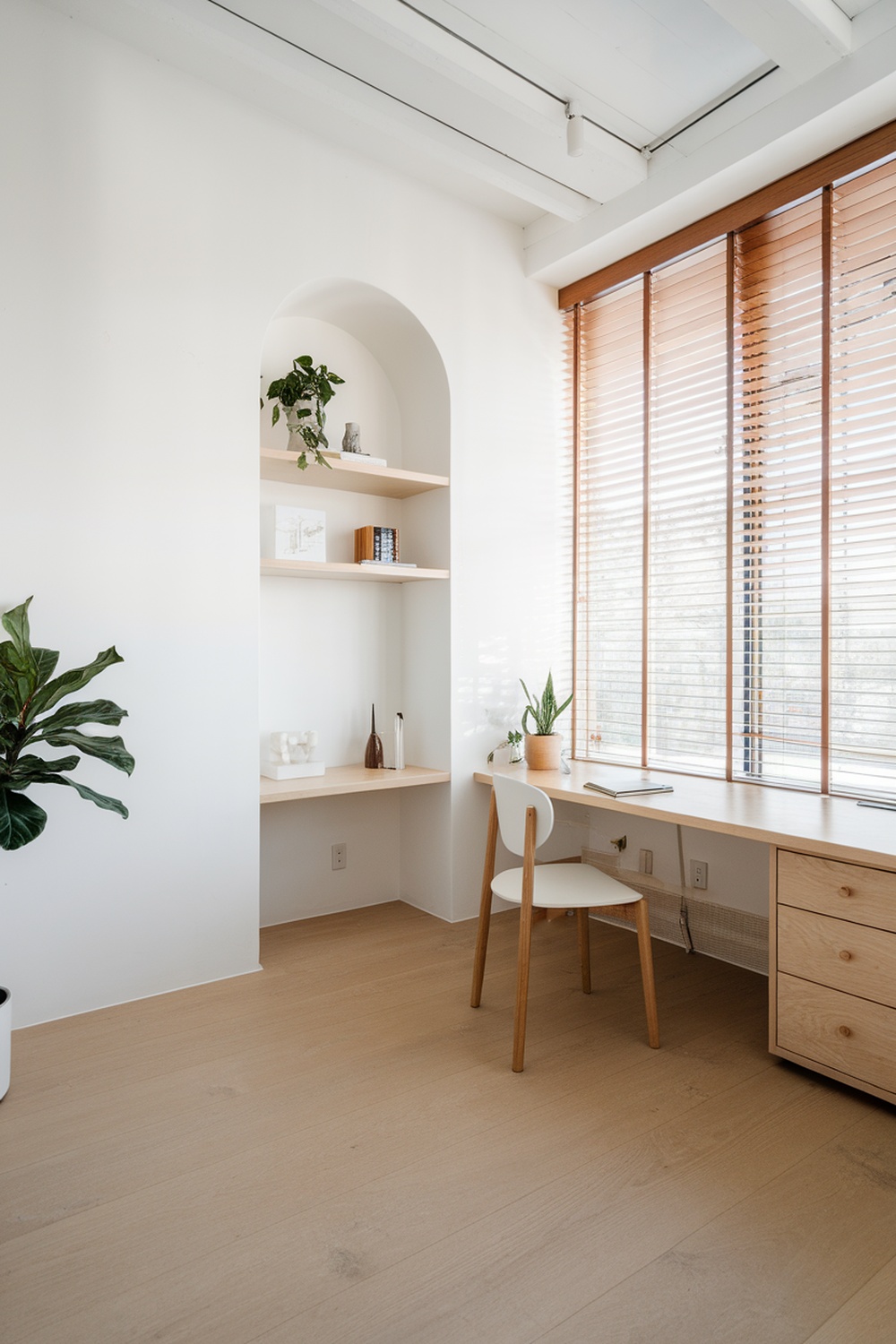 A sleek Scandinavian home office featuring a light wood desk, a simple chair, and open shelves with plants and decor.