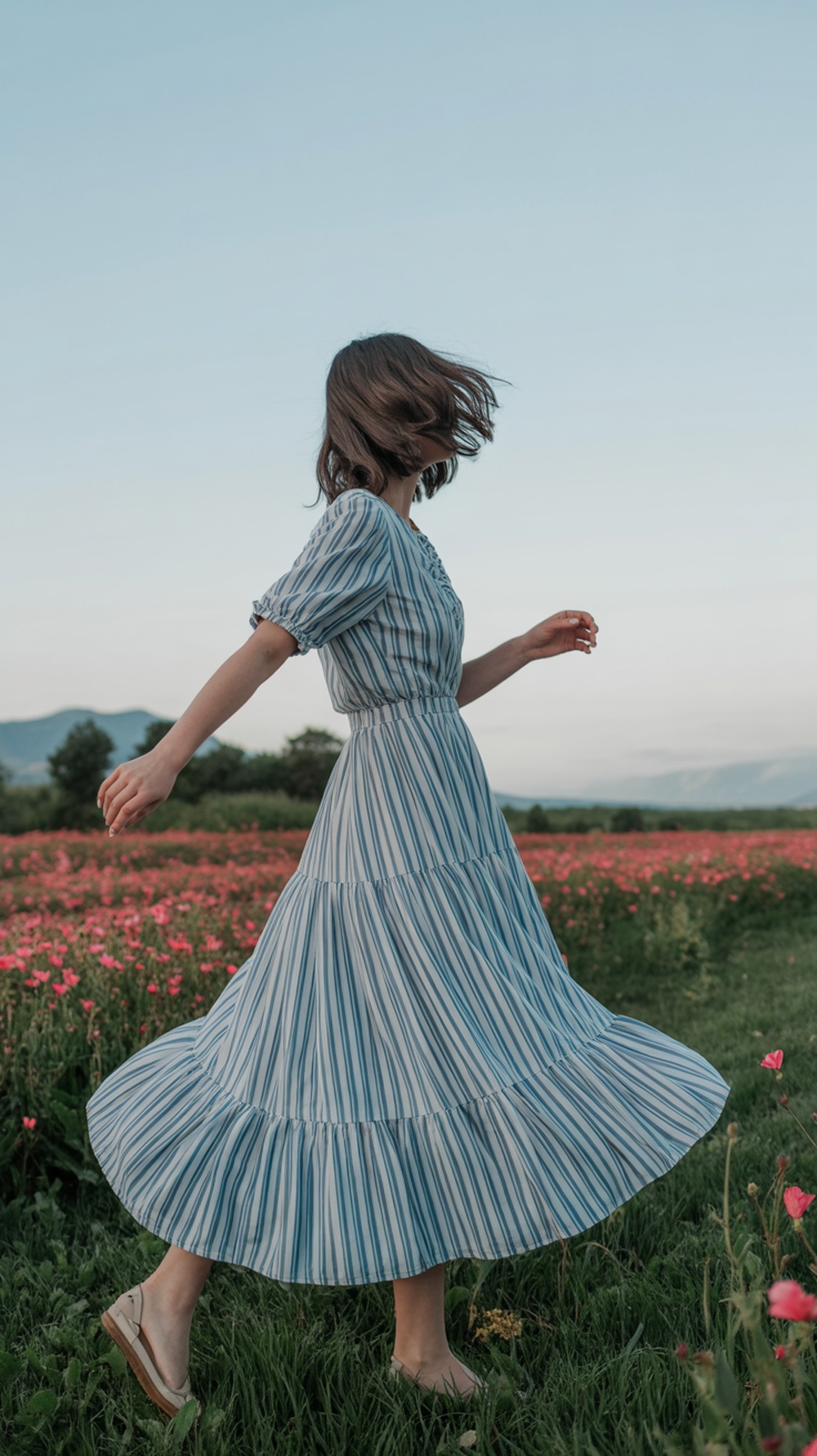 A woman in a blue and white striped maxi dress twirling in a field of flowers