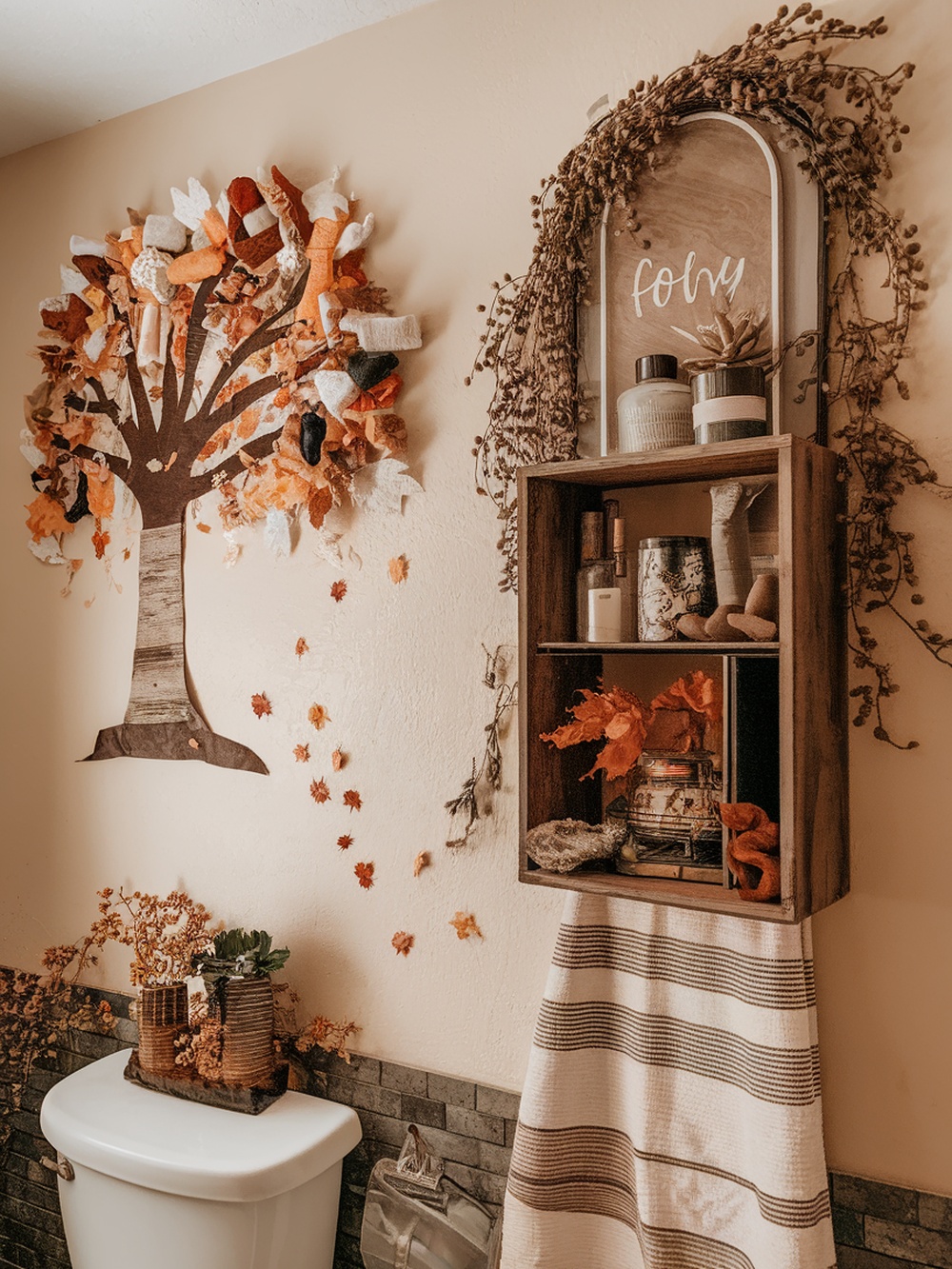 A cozy fall-themed bathroom with a leaf tree decoration and wooden shelf.