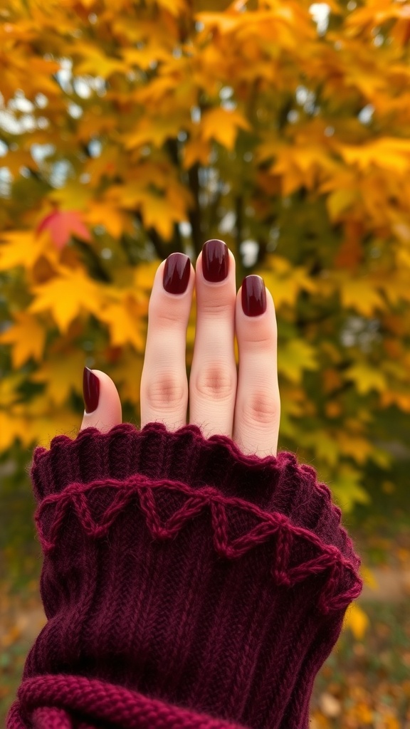 Close-up of fingernails painted with burgundy brown polish against a backdrop of autumn leaves.