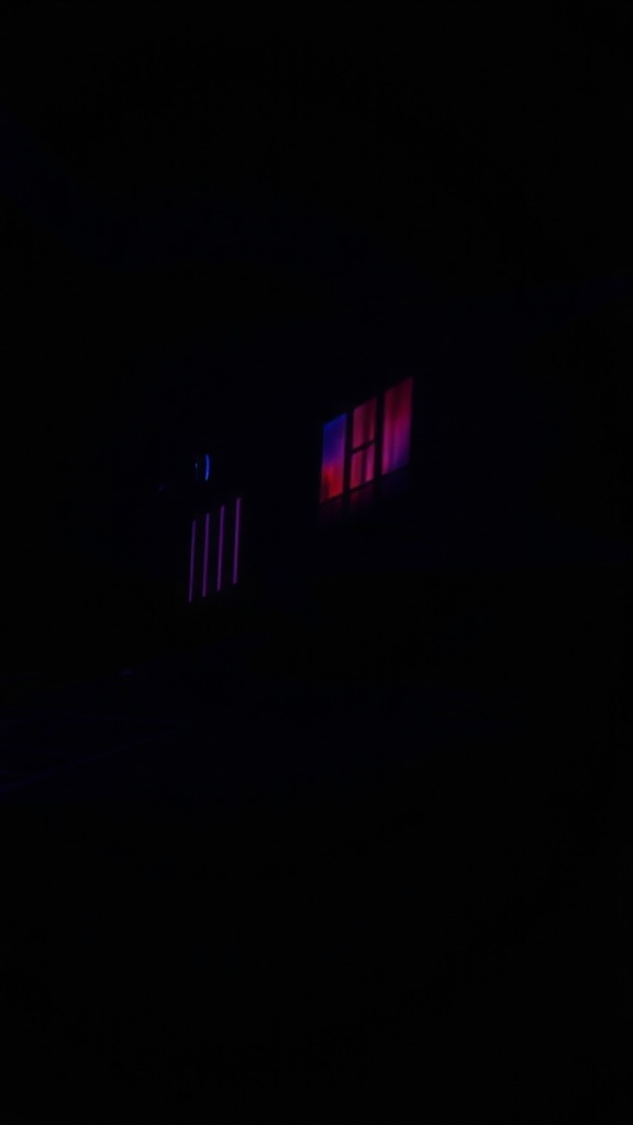 A dark scene with colorful lights visible through a window, creating an eerie atmosphere.