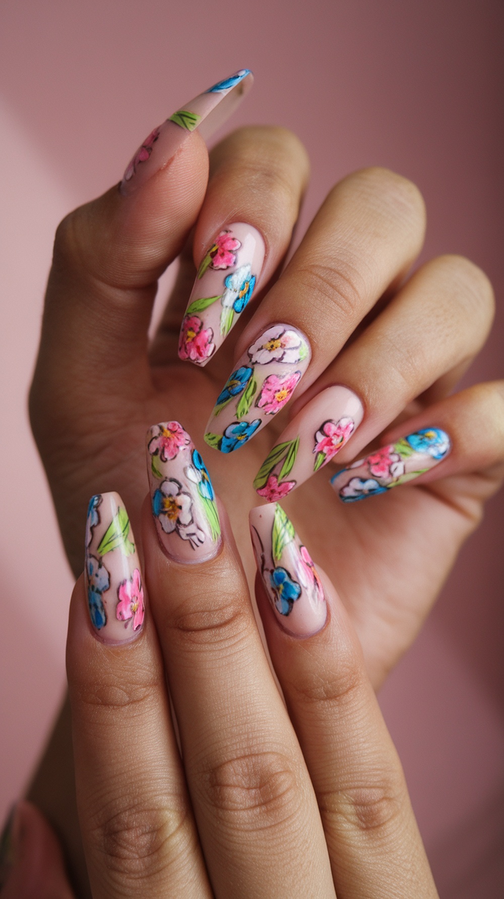 A close-up of hands with floral acrylic nail designs featuring colorful flowers on a nude background.