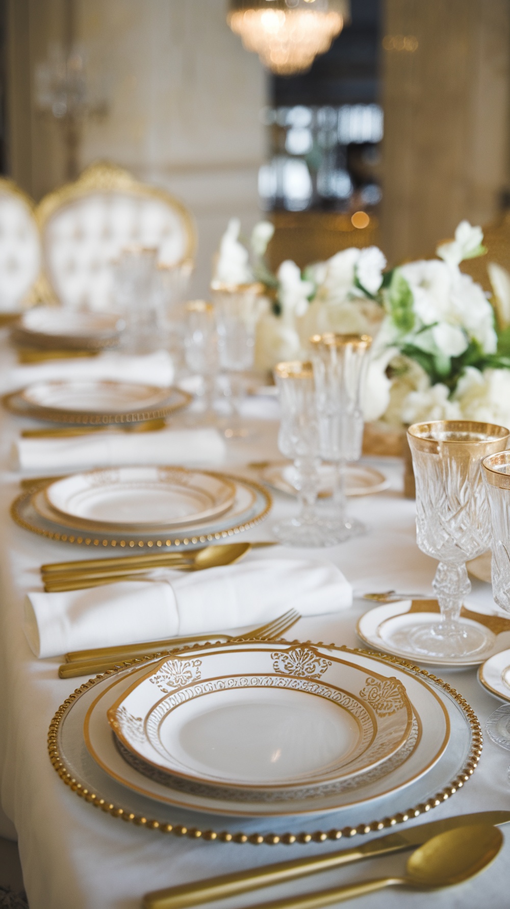 A beautifully arranged table featuring elegant tableware with gold trim, including plates, crystal glasses, and golden cutlery.