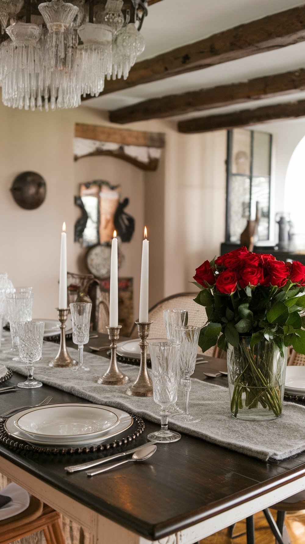A beautifully set dining table featuring a felted table runner, elegant candles, and a bouquet of red roses.
