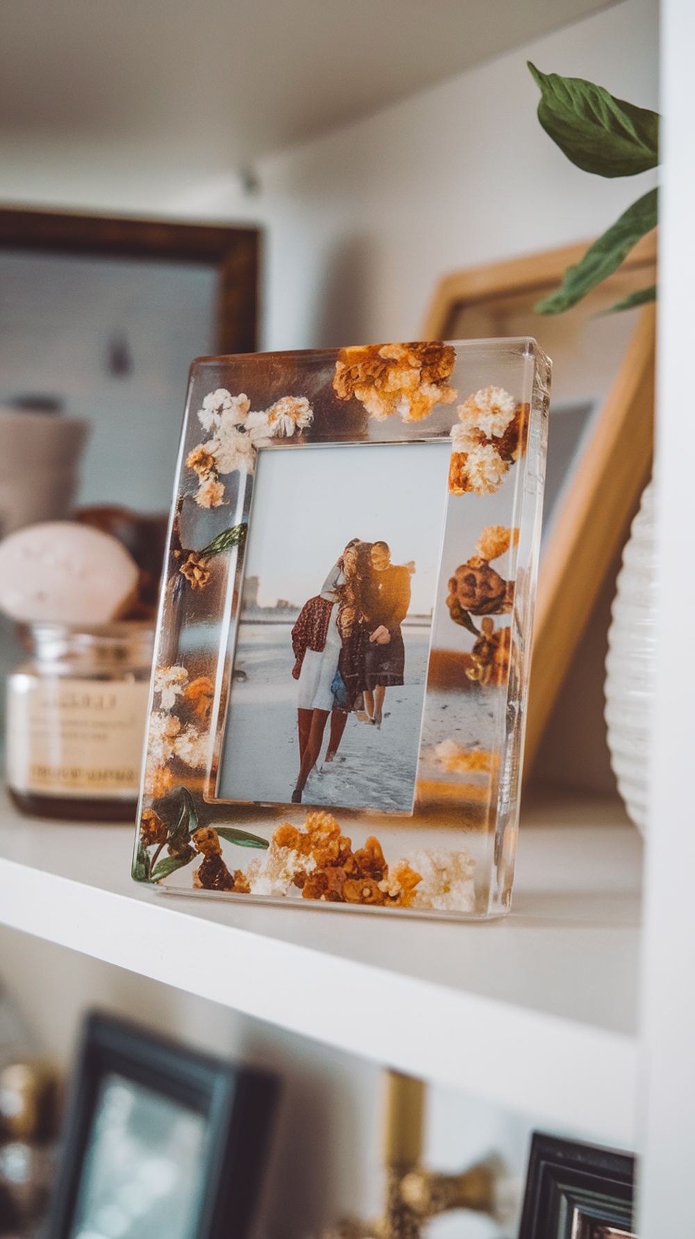 A resin photo frame with dried flowers, showcasing a photo of people walking on the beach.