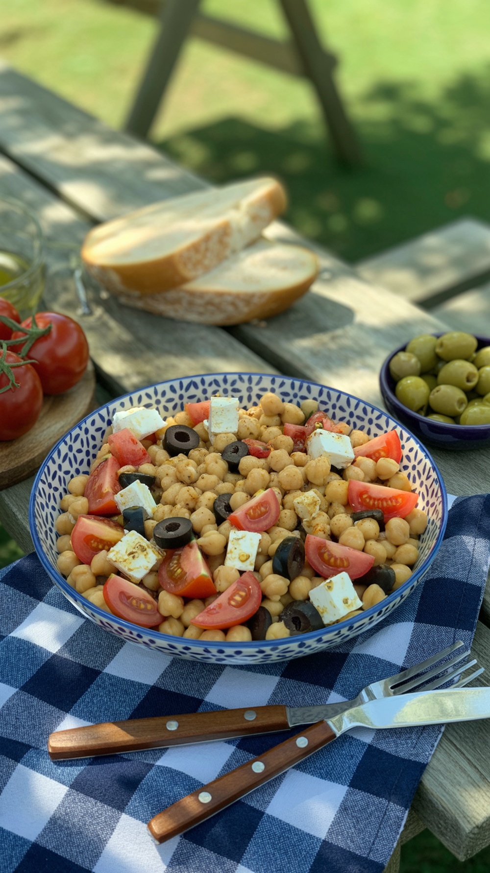 A colorful Mediterranean chickpea salad with tomatoes, olives, and feta on a picnic table.