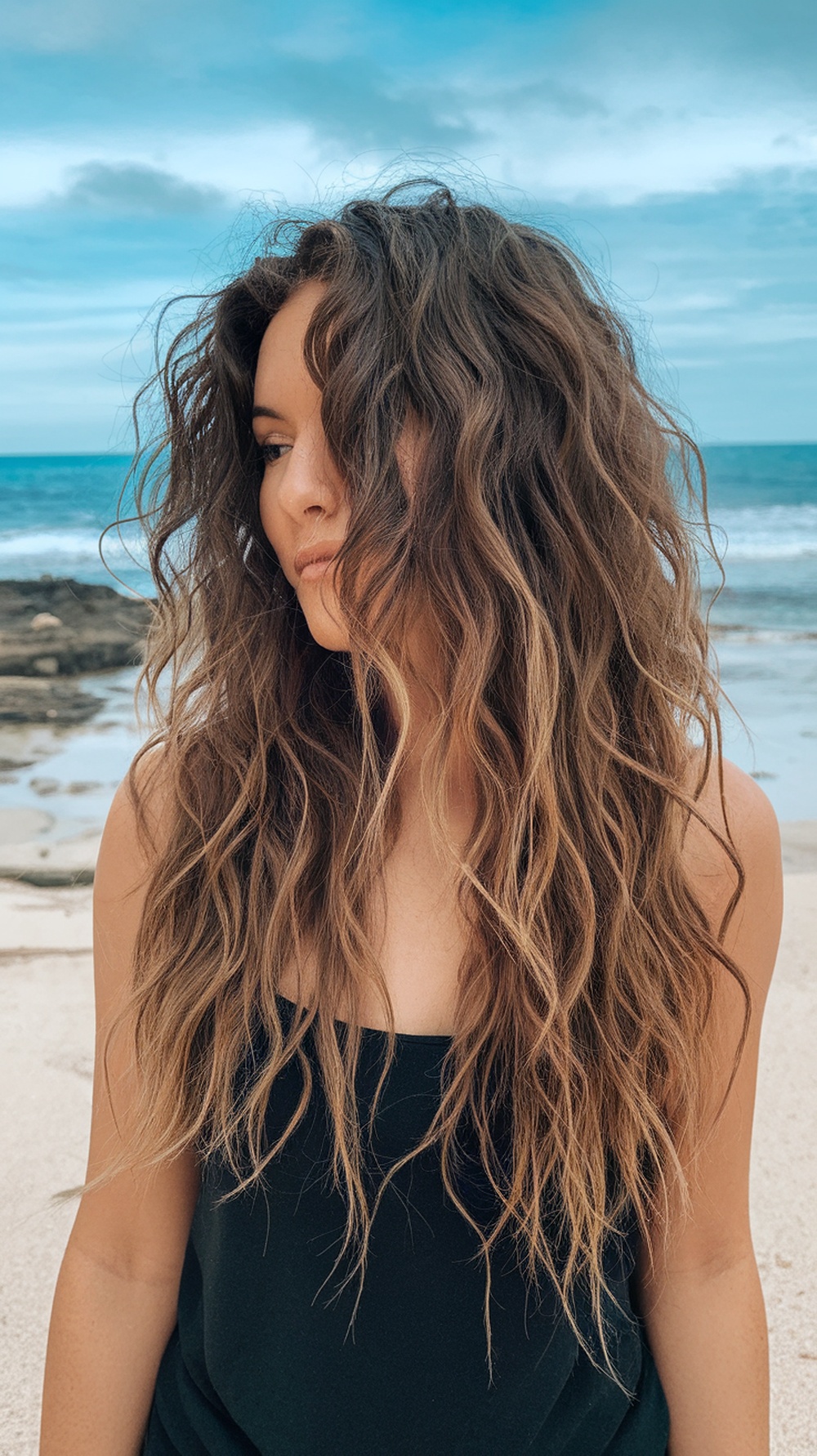 Woman with long, curly hair styled in beach waves by the ocean
