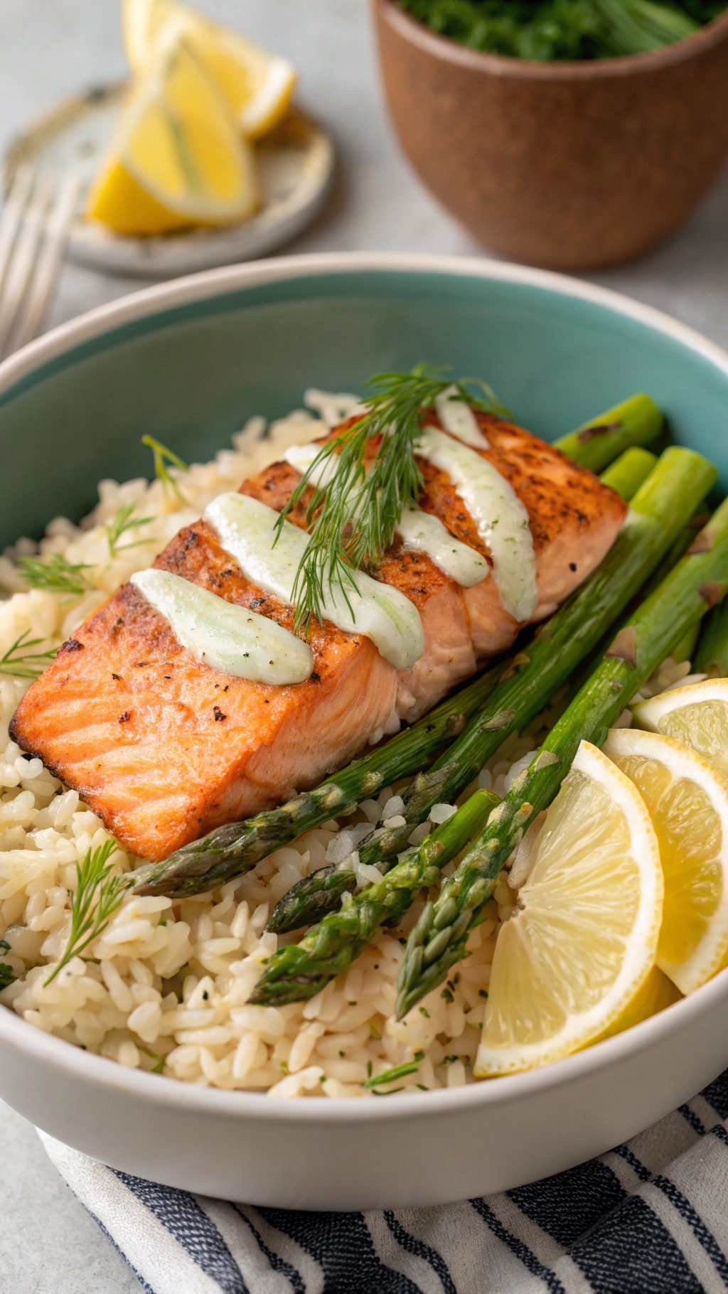 A nutritious salmon and asparagus rice bowl with creamy sauce and lemon slices.