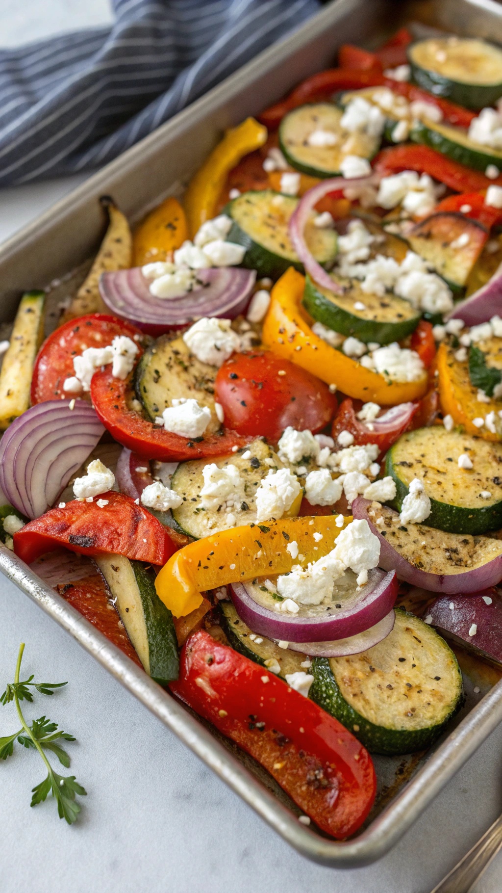 A sheet pan filled with roasted vegetables including zucchini, bell peppers, red onions, and topped with crumbled feta cheese.