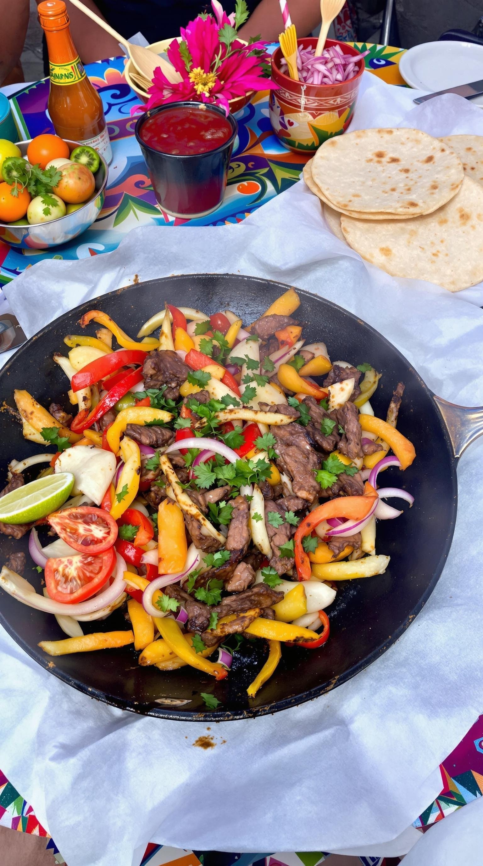 A colorful plate of beef fajitas with peppers, garnished with cilantro and lime, served with tortillas.