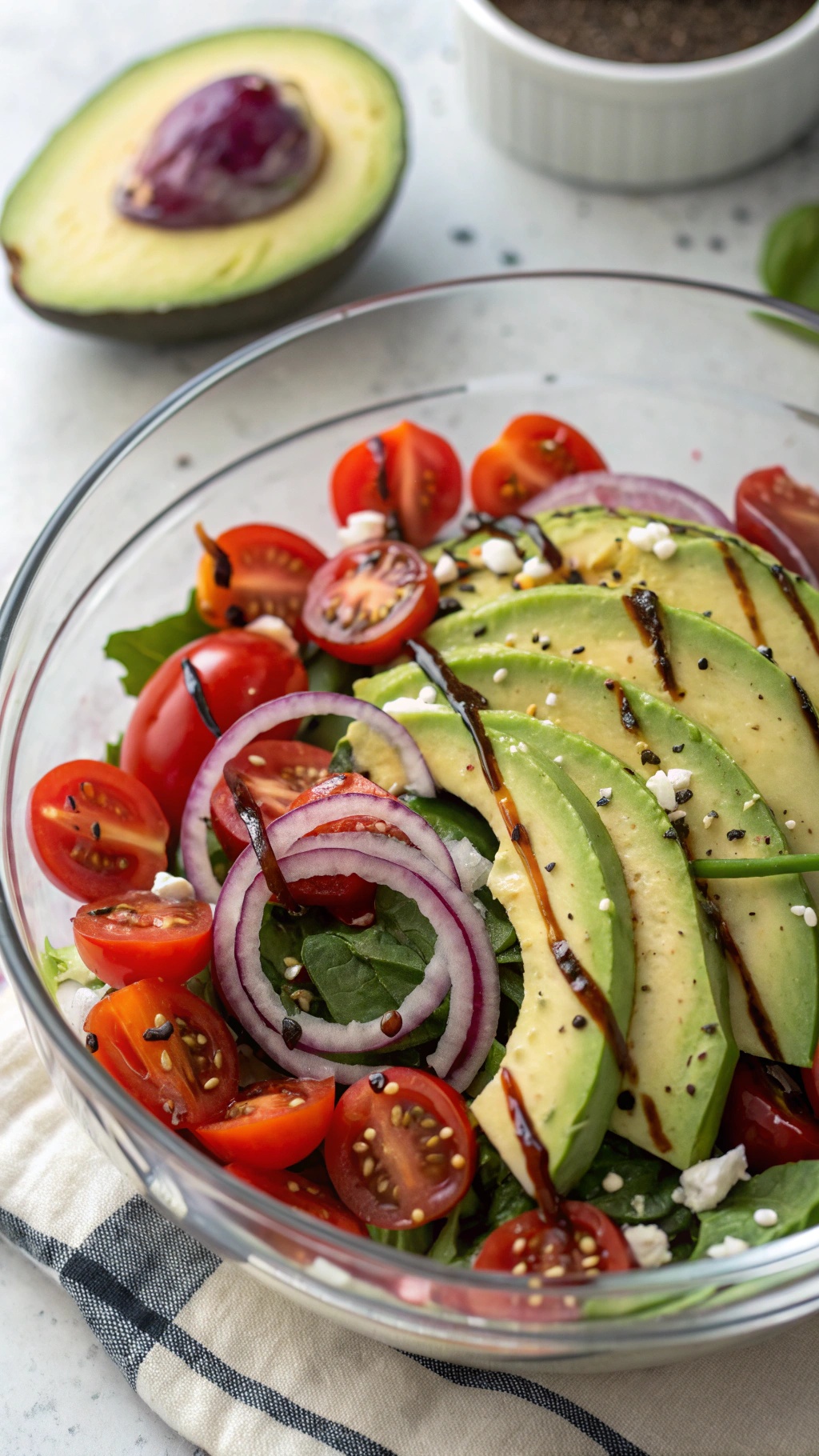 A vibrant salad featuring sliced avocado, cherry tomatoes, red onion, and mixed greens, drizzled with balsamic glaze.