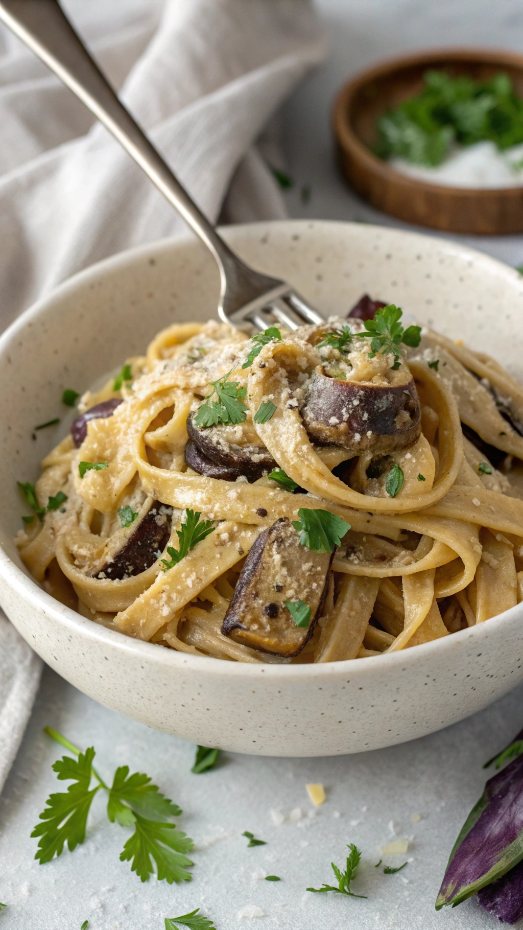 A bowl of creamy vegan eggplant Alfredo pasta garnished with parsley.