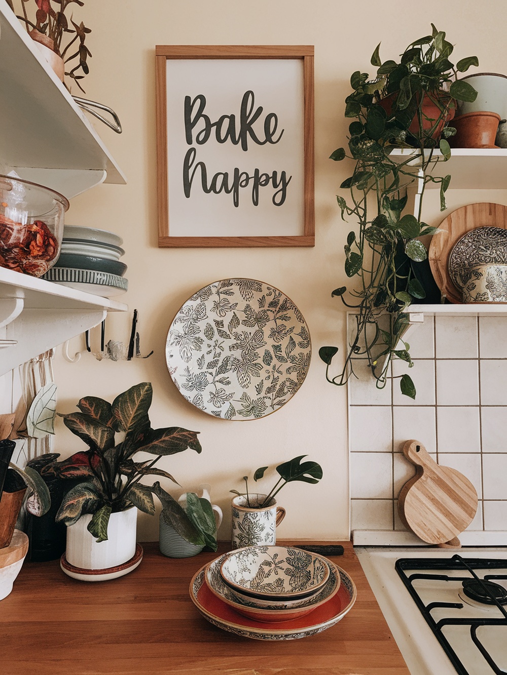 A cozy kitchen corner with a framed sign, decorative plates, and plants.