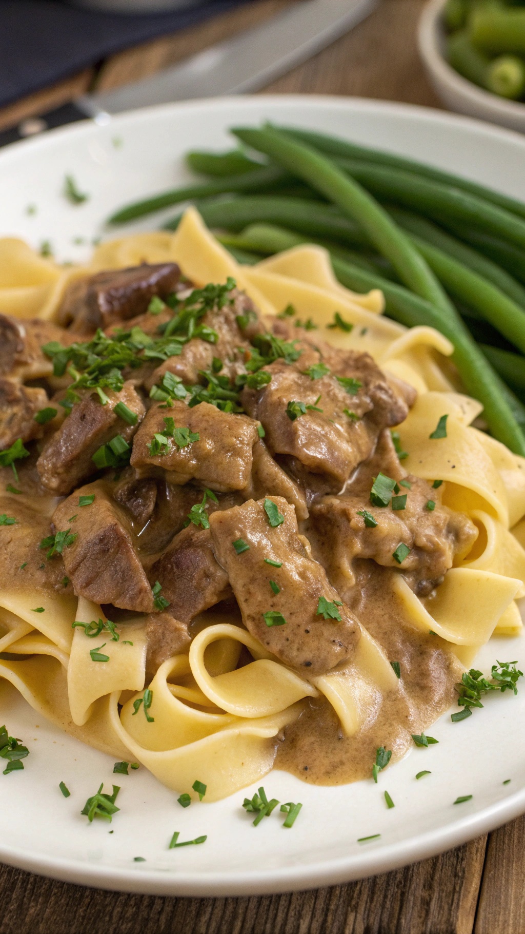 A plate of beef stroganoff served over noodles with green beans on the side.