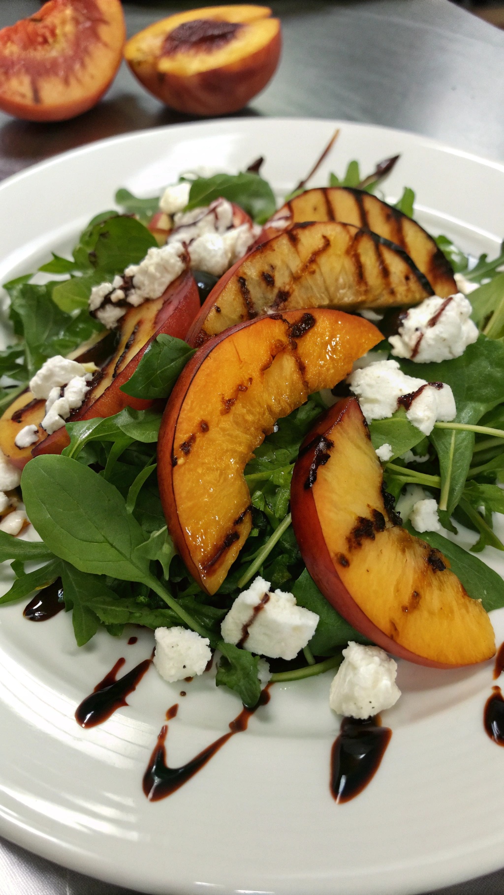 A vibrant grilled peach salad with goat cheese, arugula, and balsamic reduction on a white plate.