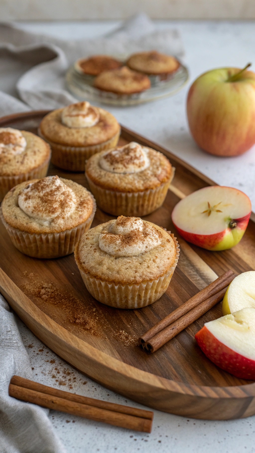 Apple cinnamon protein muffins on a wooden platter with sliced apples and cinnamon sticks.