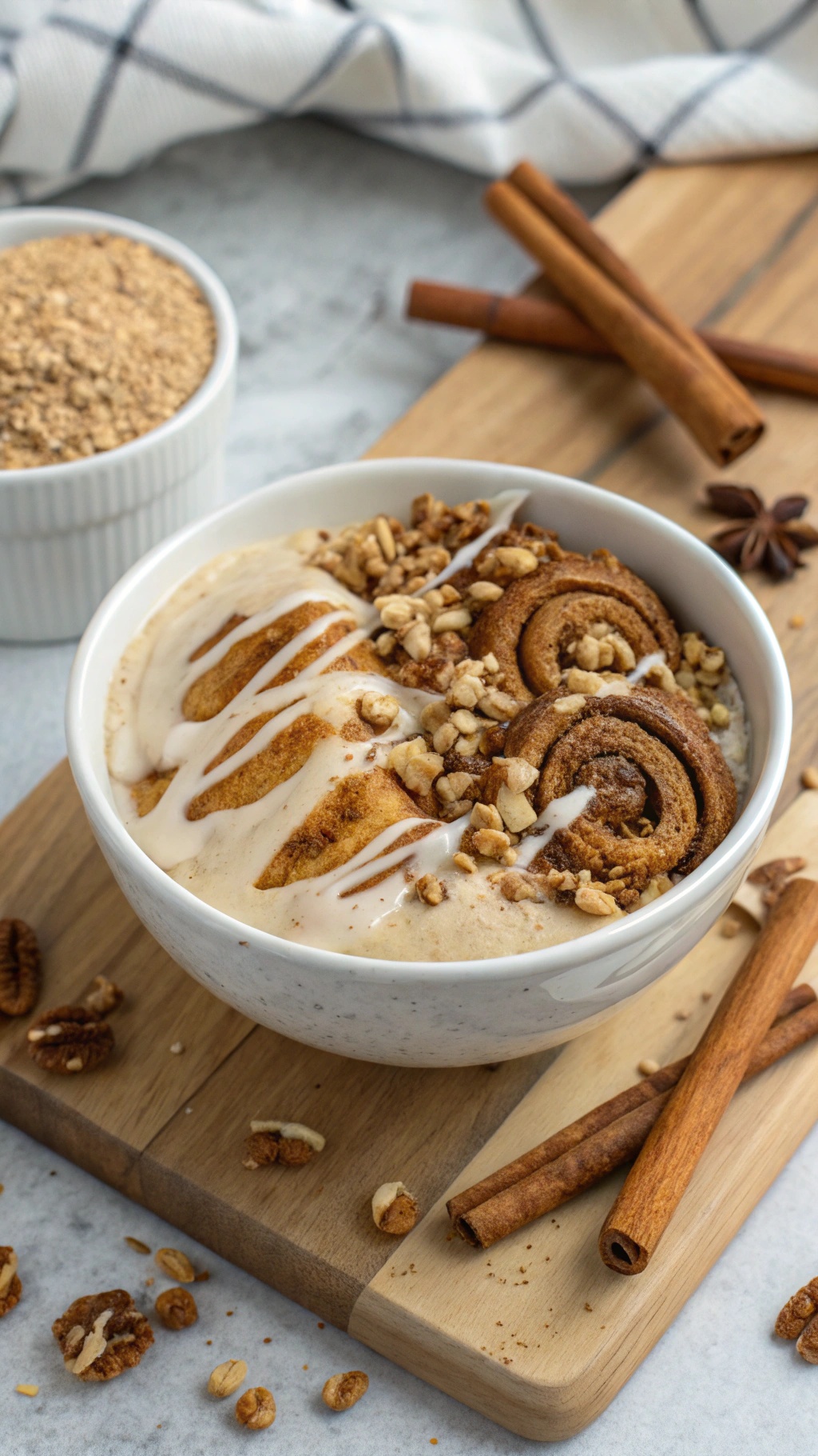 A cinnamon roll inspired smoothie bowl topped with sliced cinnamon rolls, granola, and icing on a wooden board.