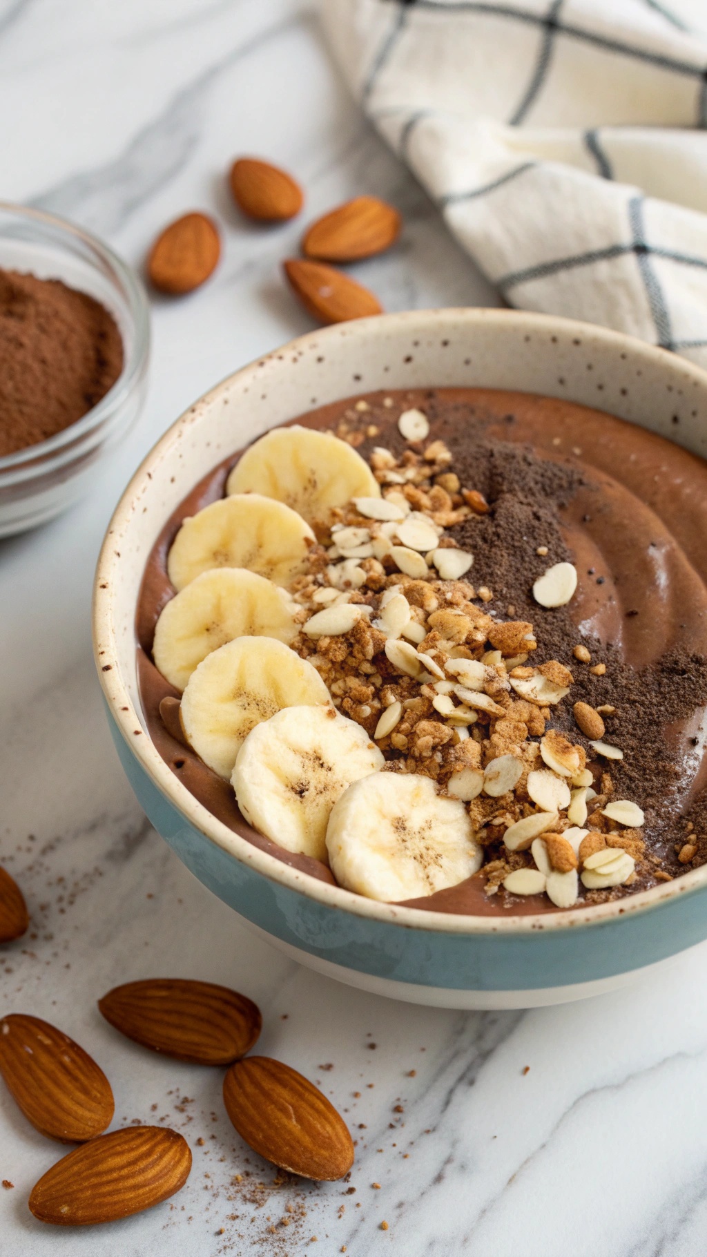 A delicious chocolate almond smoothie bowl topped with banana slices, granola, and almonds.