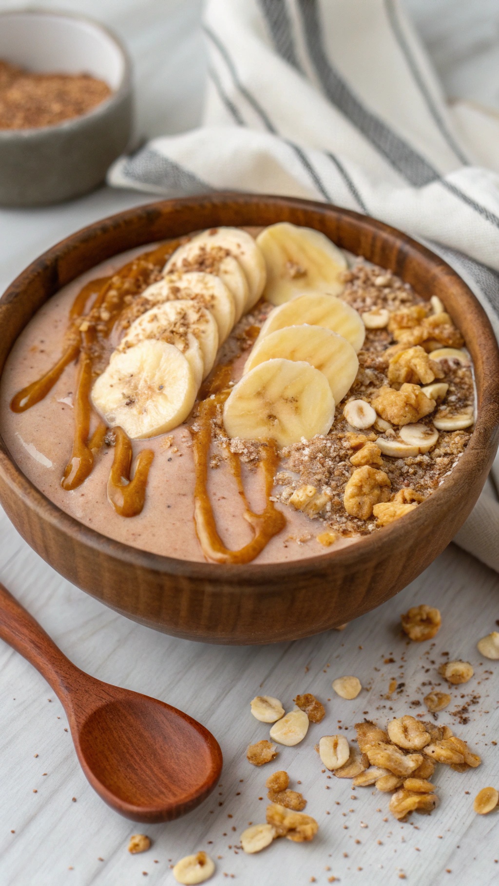 A smoothie bowl topped with banana slices, almond butter, and granola in a wooden bowl.