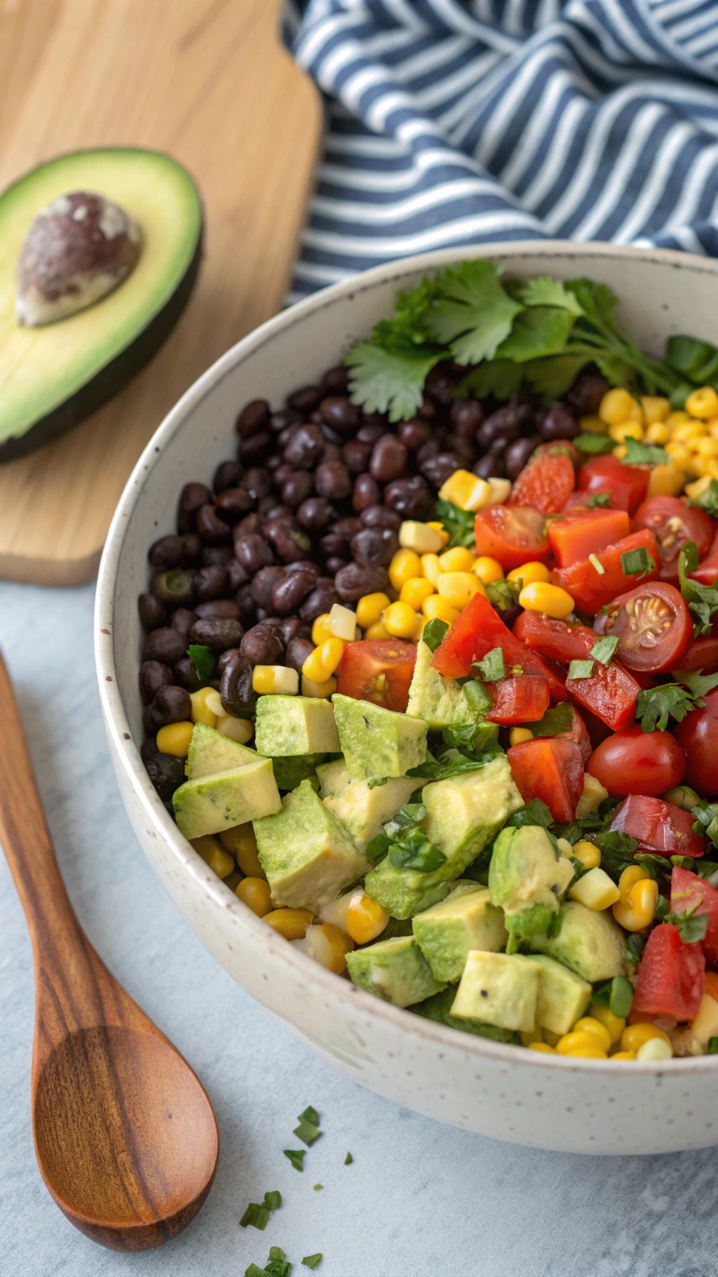 A bowl of colorful black bean and corn salad with diced avocado, cherry tomatoes, and fresh cilantro.