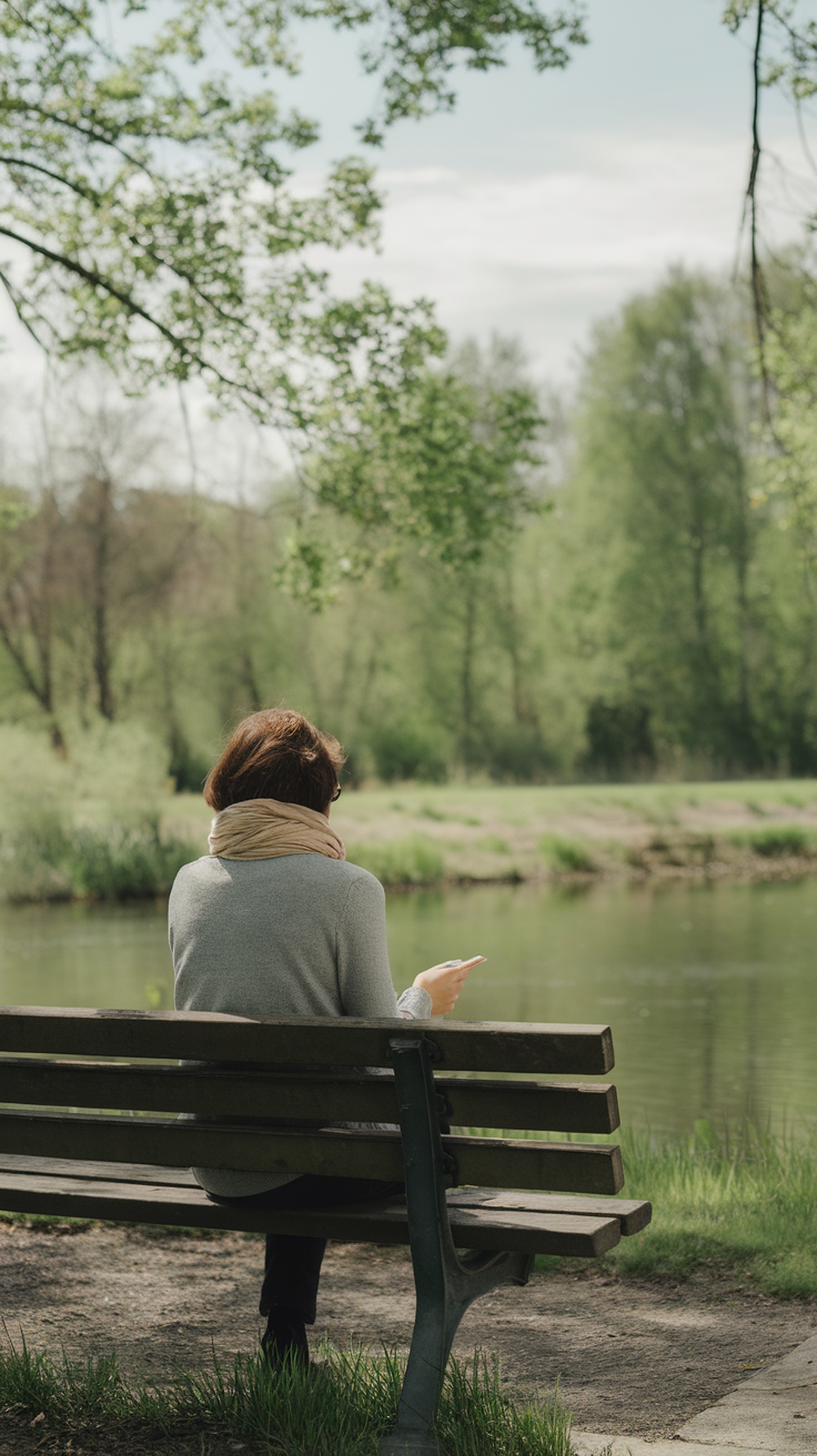 A person sitting on a bench by a lake, enjoying nature and taking a break from digital devices.
