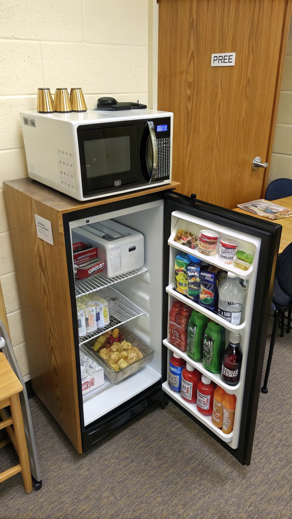 A compact kitchenette setup featuring a microwave and a mini fridge filled with snacks and drinks.