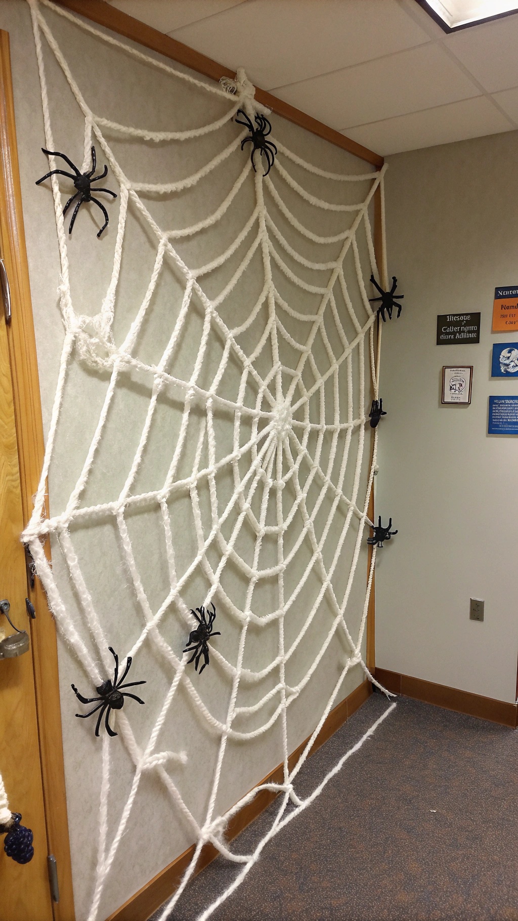 A large white spider web made of yarn on a door, with black plastic spiders attached.