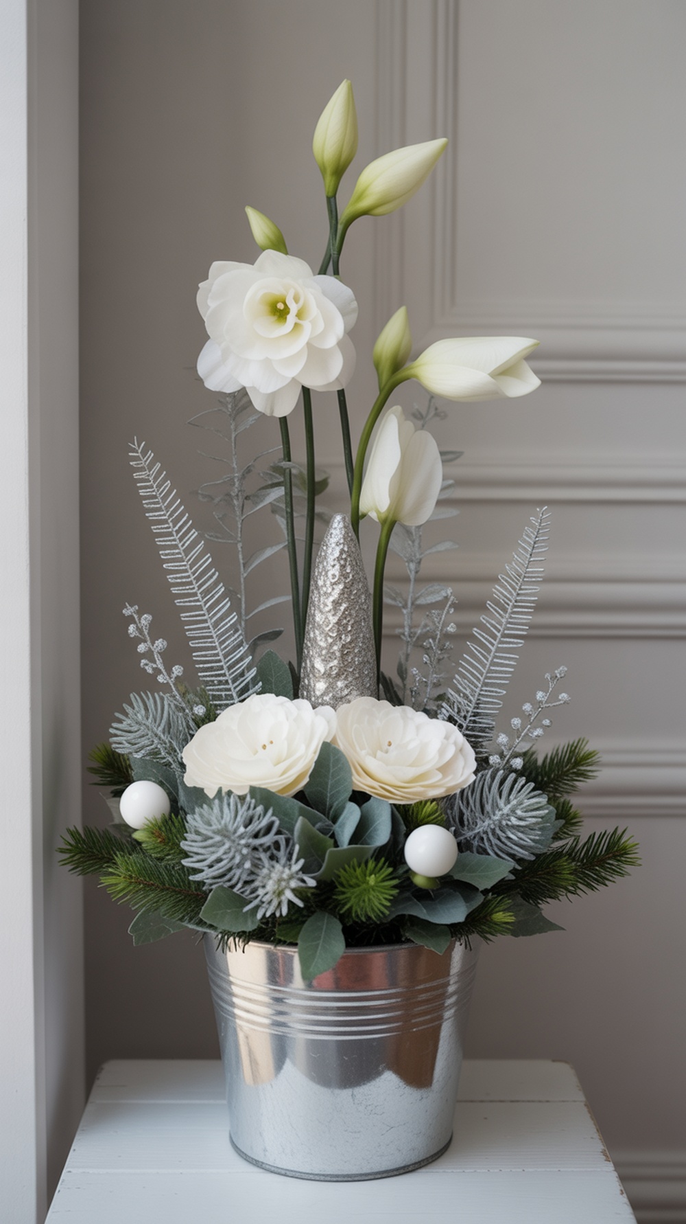 A silver planter filled with white flowers and greenery, featuring a silver decorative cone.