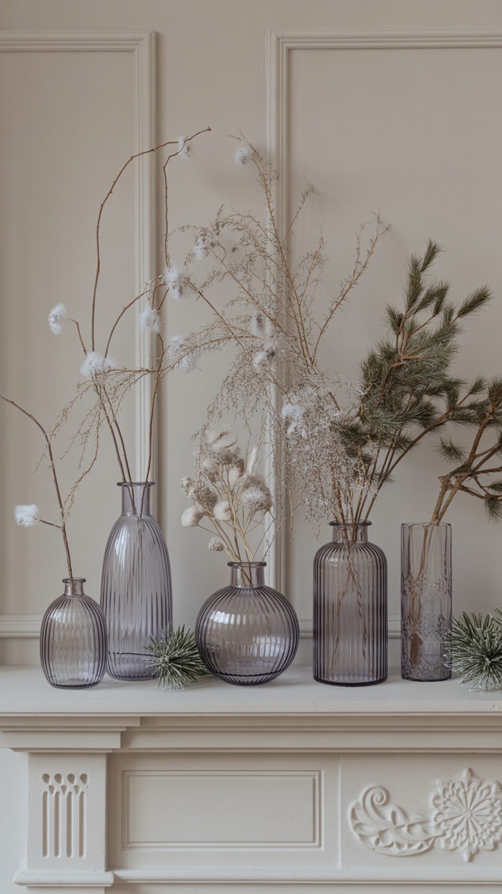 A collection of frosted glass vases with branches and decorative elements on a mantel.