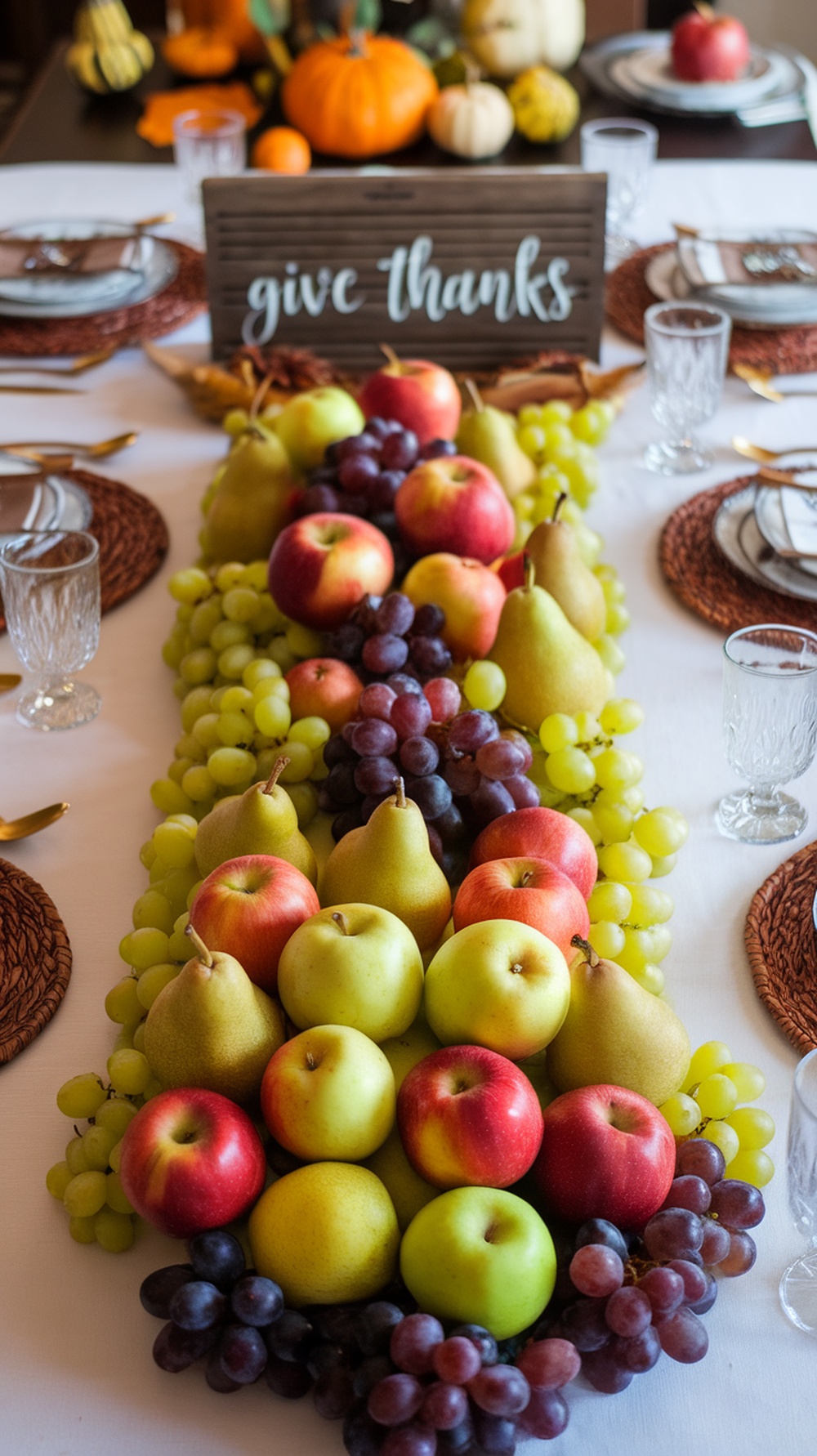 A Thanksgiving table with a fruit display featuring apples, pears, and grapes, along with a sign that says 'give thanks'.