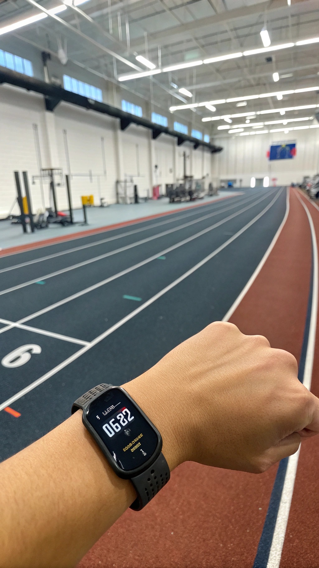A fitness tracker on a wrist displaying stats at a gym track.