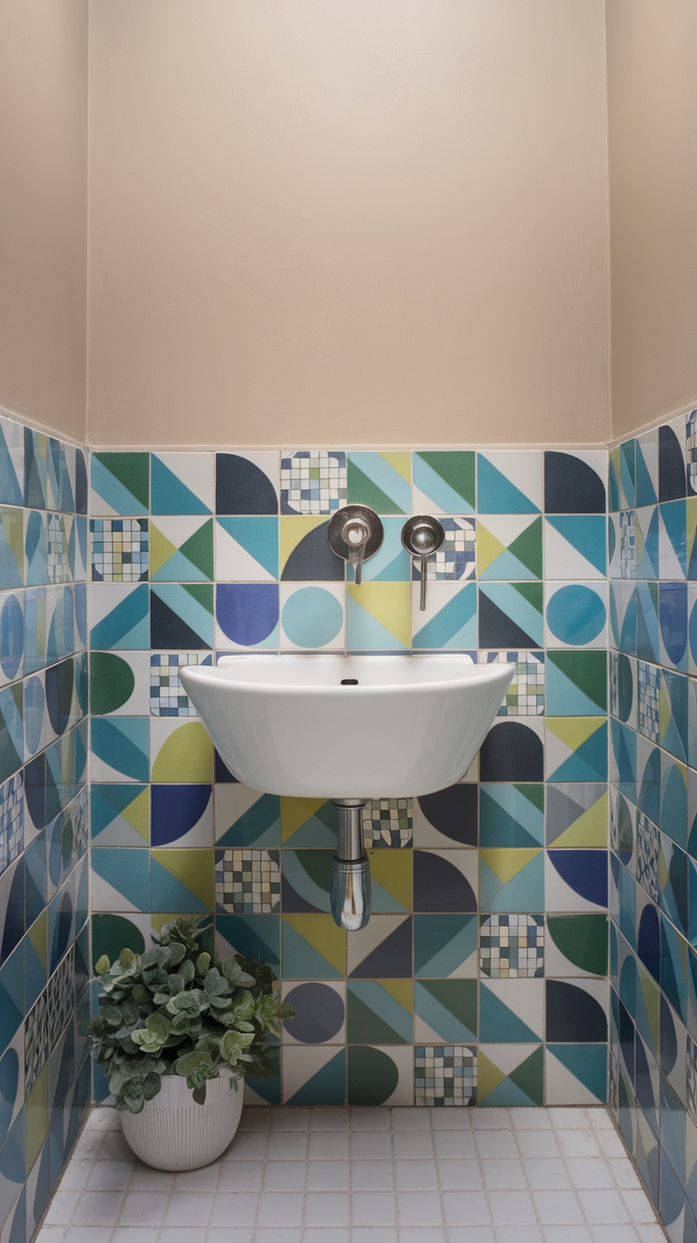 A small bathroom featuring colorful mosaic tiles in geometric patterns, with a white sink and a potted plant.
