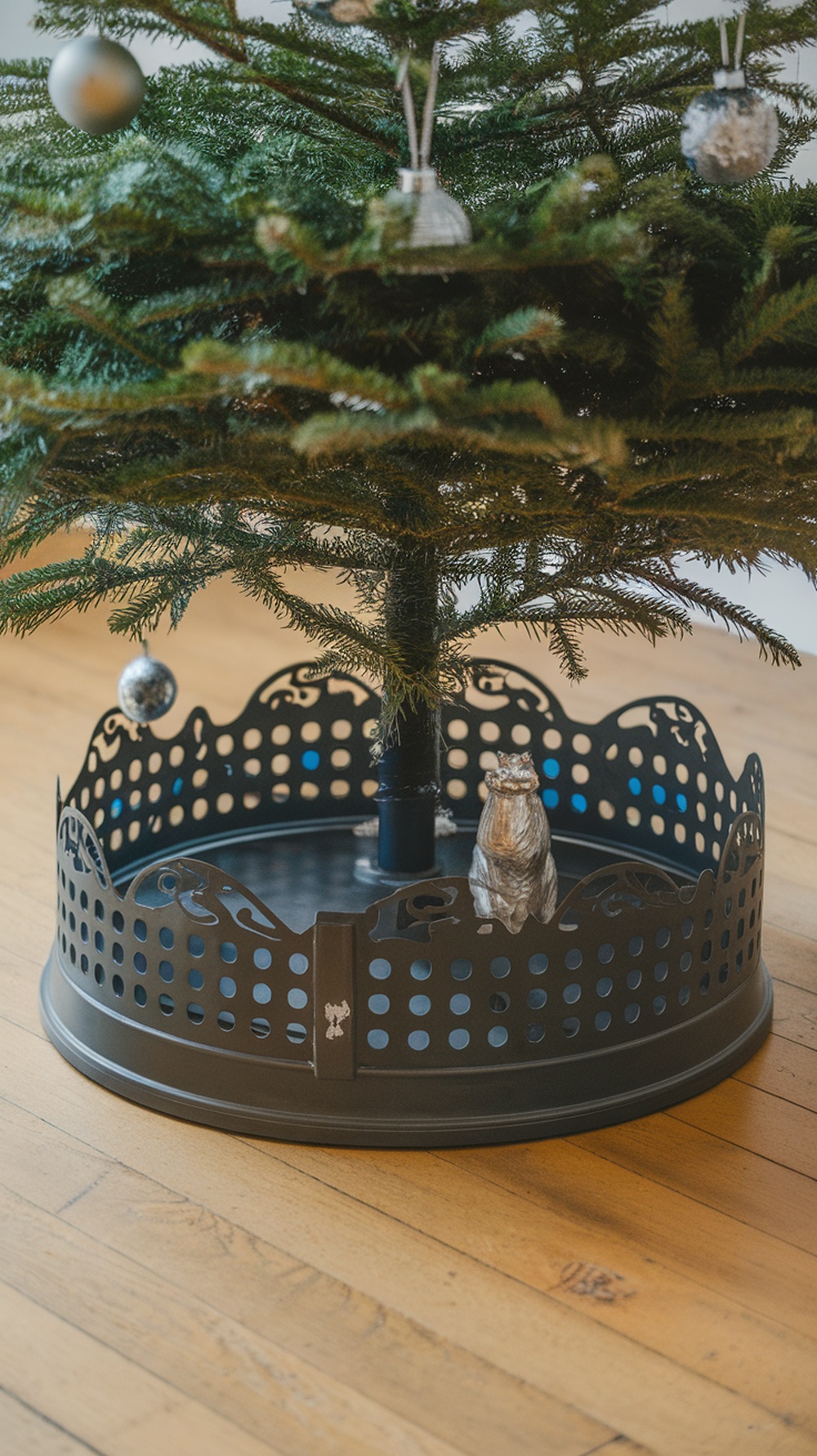 A stylish black tree base with a decorative design, featuring a cat figurine, under a Christmas tree.