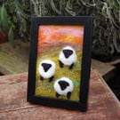 Colourful sheep wool painting.  Needlefelt picture of three sheep and flowers