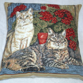 A ginger cat and tabby cat sitting in the window with pots of geraniums cushion 