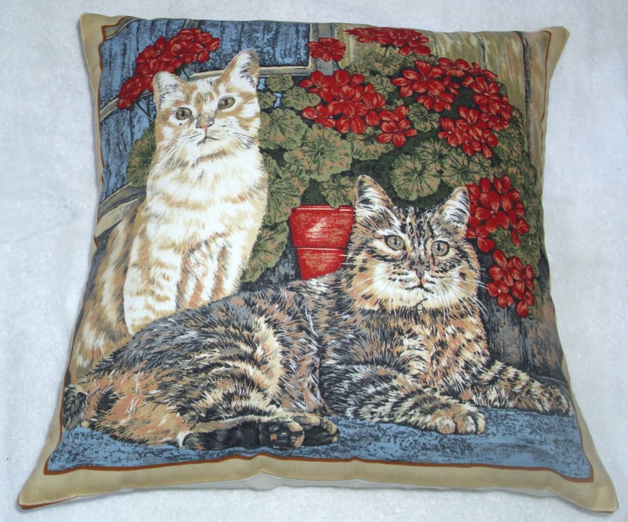 A ginger cat and tabby cat sitting in the window with pots of geraniums cushion 