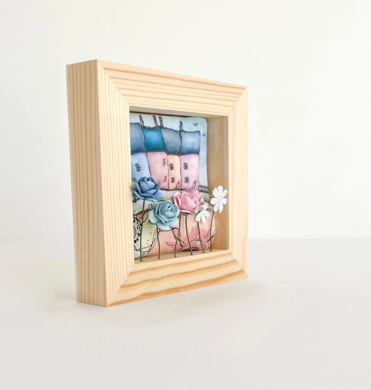 Little row of fabric houses with paper flowers, in a small wooden frame