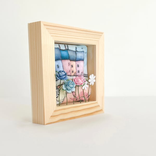 Little row of fabric houses with paper flowers, in a small wooden frame
