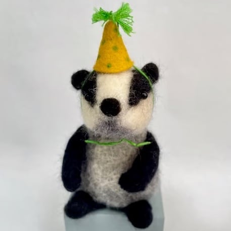 Handcrafted needle felted badger with removable party hat on a wooden box
