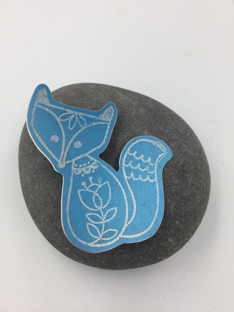 Anodised aluminium silver fox brooch on turquoise background