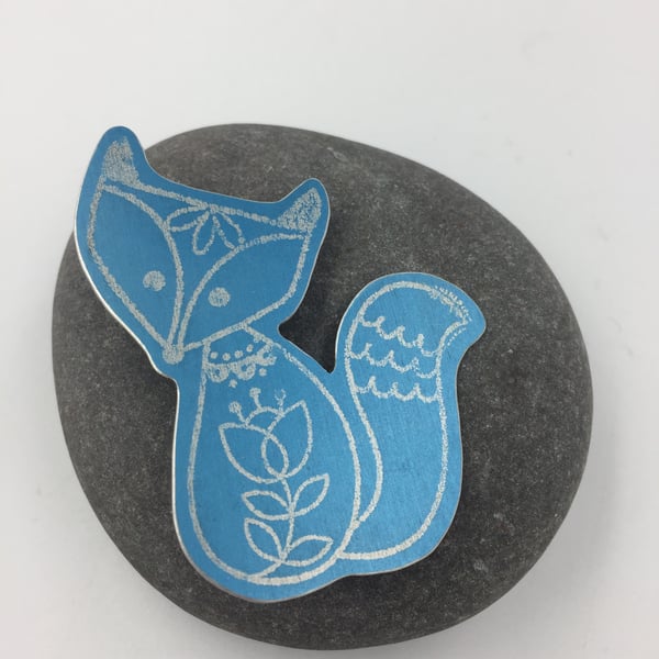 Anodised aluminium silver fox brooch on turquoise background