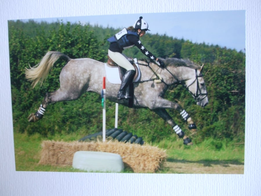 Photographic greetings card of a grey dapple horse and rider going over a jump.
