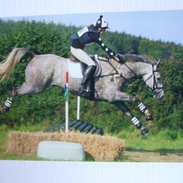 Photographic greetings card of a grey dapple horse and rider going over a jump.