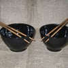 A pair of noodle bowls with chopsticks.