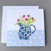 Jug of red tulips in a blue and white patterned jug on spotty tablecloth card